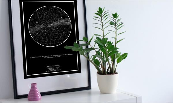 Imagem de quadro do Mapa do Céu preto encostado na parede, ao lado de um vaso com planta e vaso rosa