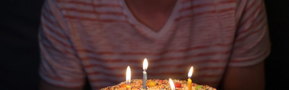 bolo de aniversário com velas e homem ao fundo ilustrando a matéria de presente de aniversario para namorado