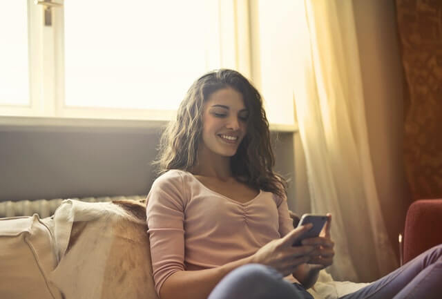 garota olha para celular sorrindo, ilustrando um namoro à distância